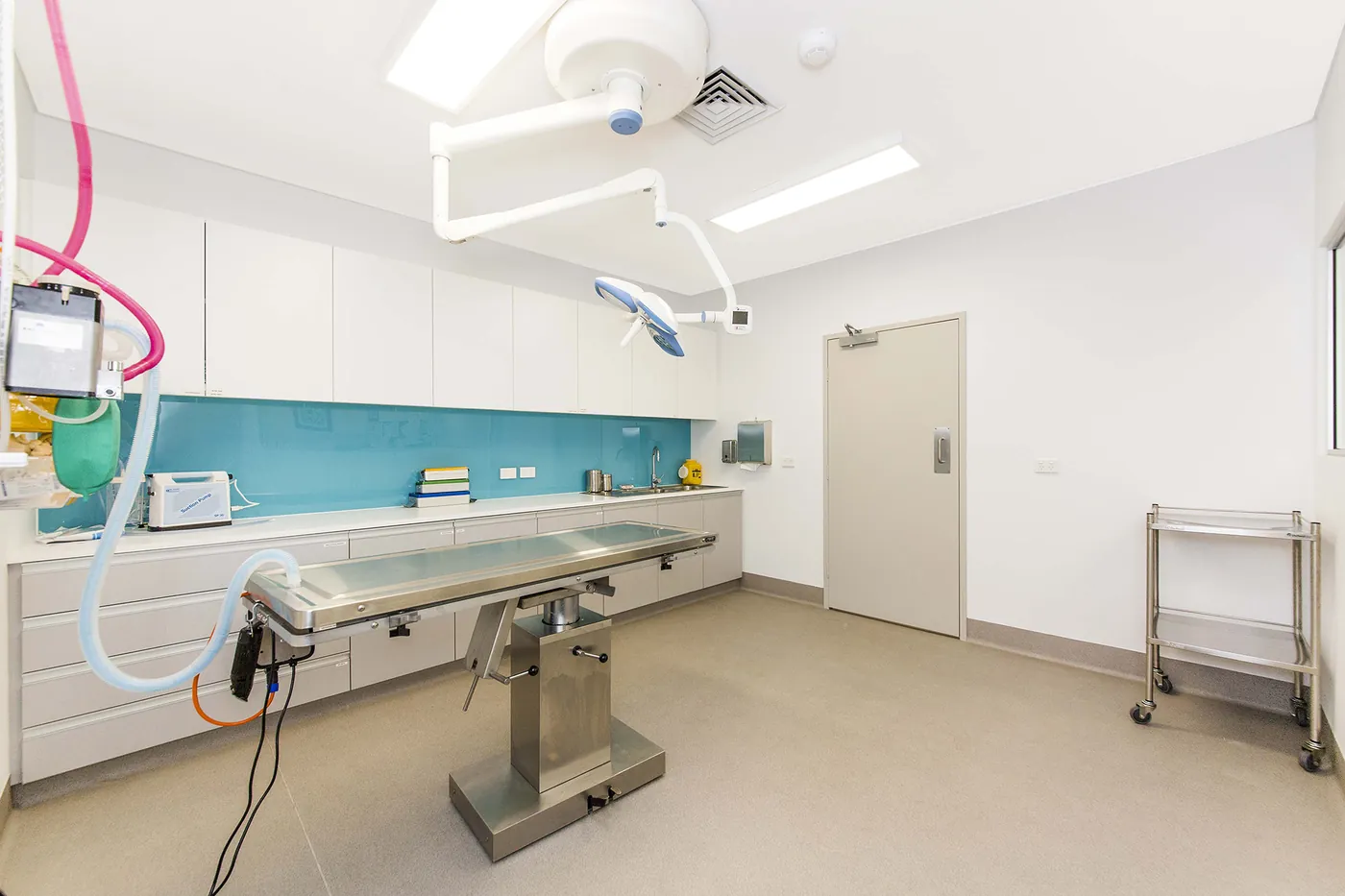 Emergency Vet Hospital — Surgical theatre with operating lights, stainless table and teal splashback.